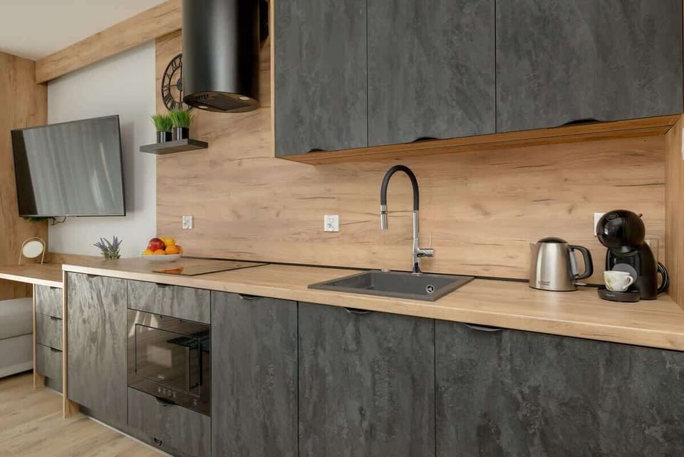 A modern kitchen corner with a black sink, wooden countertop, and overhead cabinets in a textured finish.