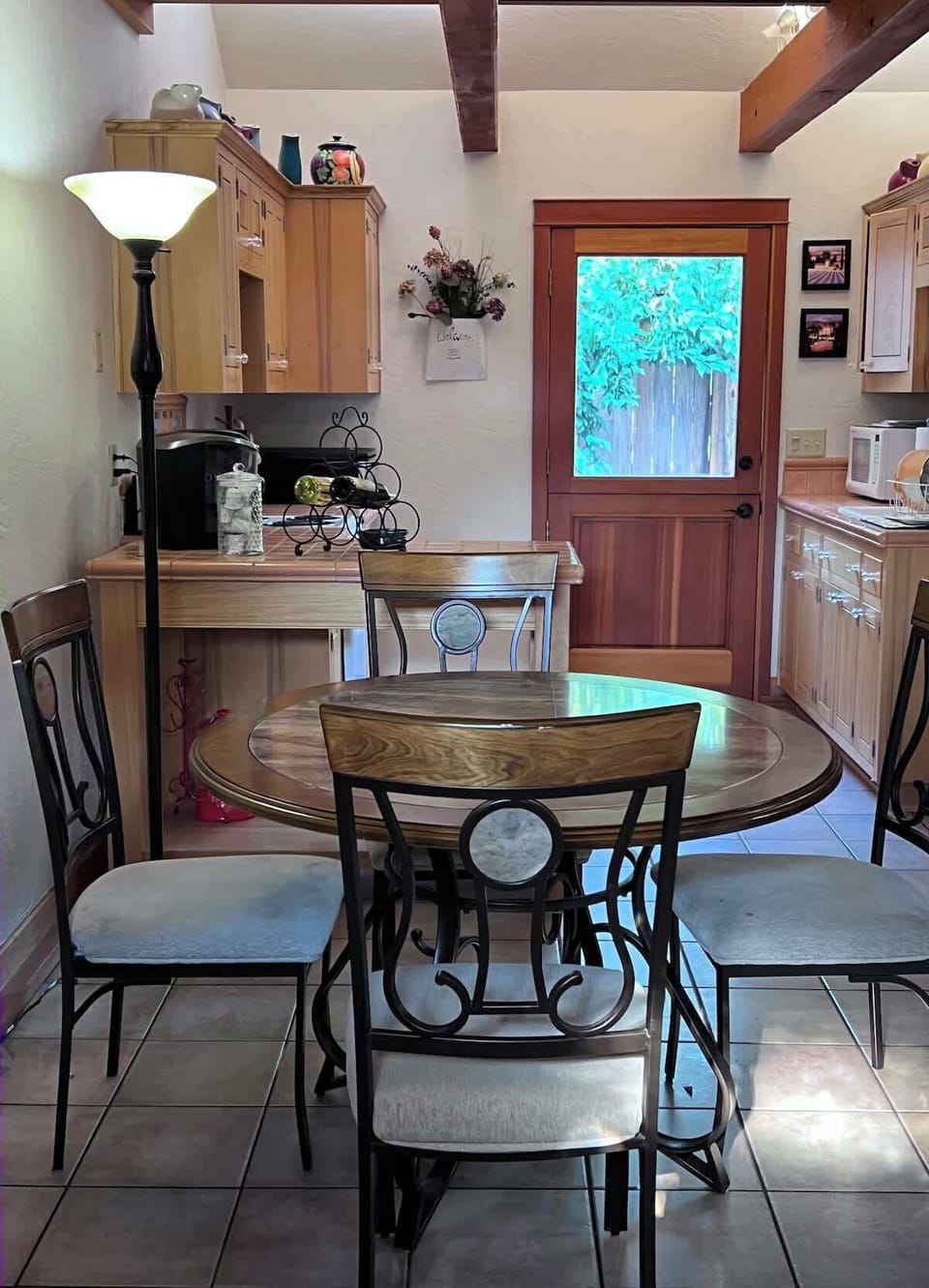 Bright and welcoming dining area featuring a round wood table with seating for four, set just off the kitchen. Natural light from the glass back door and exposed ceiling beams create a warm inviting atmosphere, perfect for meals or morning coffee.