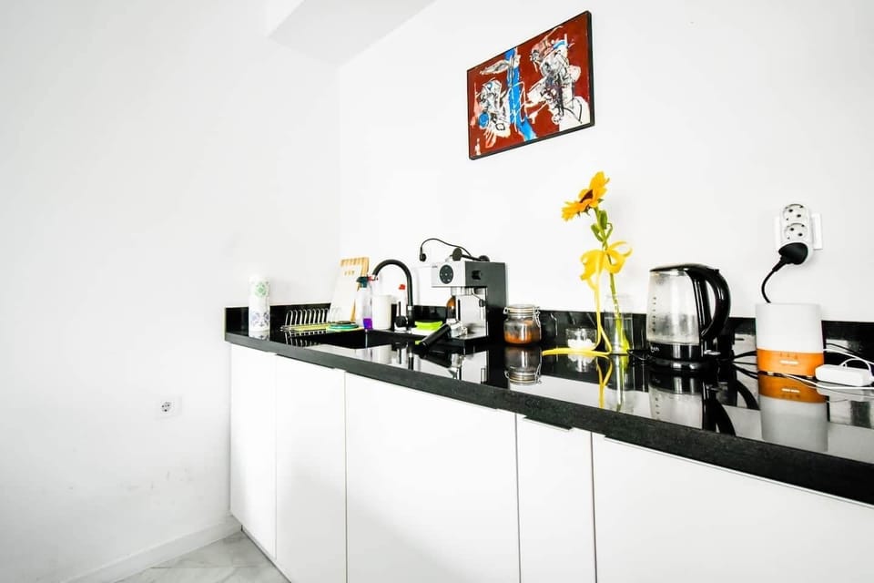 Modern kitchen area with a black countertop, white cabinets, and stainless-steel appliances against a wall adorned with colorful art.