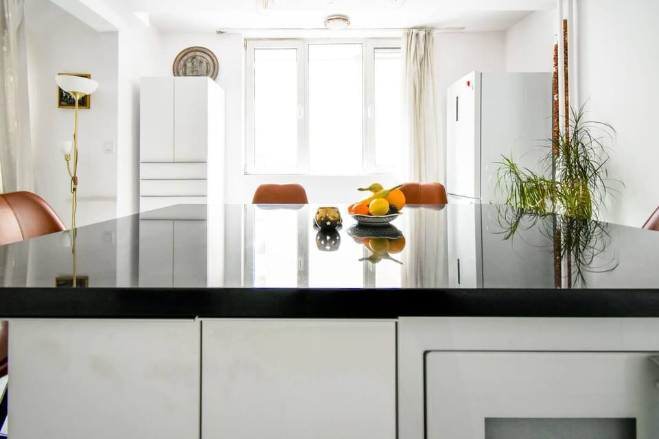 View of the modern kitchen countertop seen from the dining area, with shiny black surfaces reflecting a bowl of fresh fruit.
