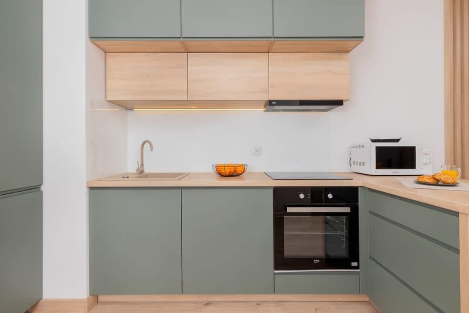 A contemporary kitchen with light grey cabinetry and wooden accents. It includes an oven and ample storage space, designed with clean lines and functionality in mind.