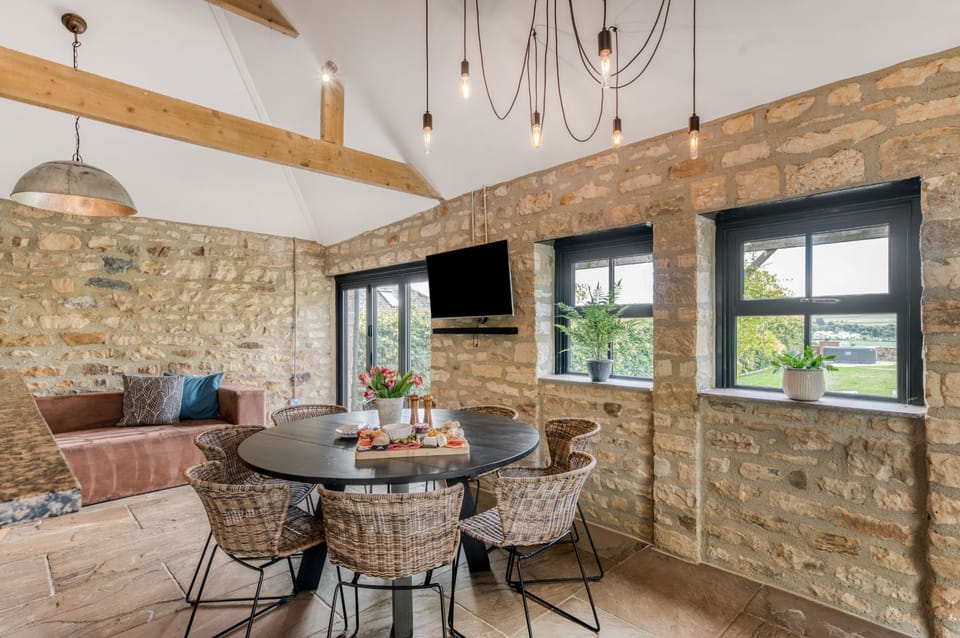 Rustic games room with TV, sofa, round dining table and exposed stone walls in The Farmhouse at Greenbank Barns.