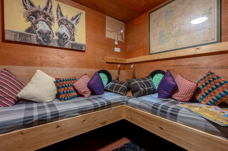 Cosy snug with built-in seating, colourful cushions, porthole windows and rustic wooden walls.