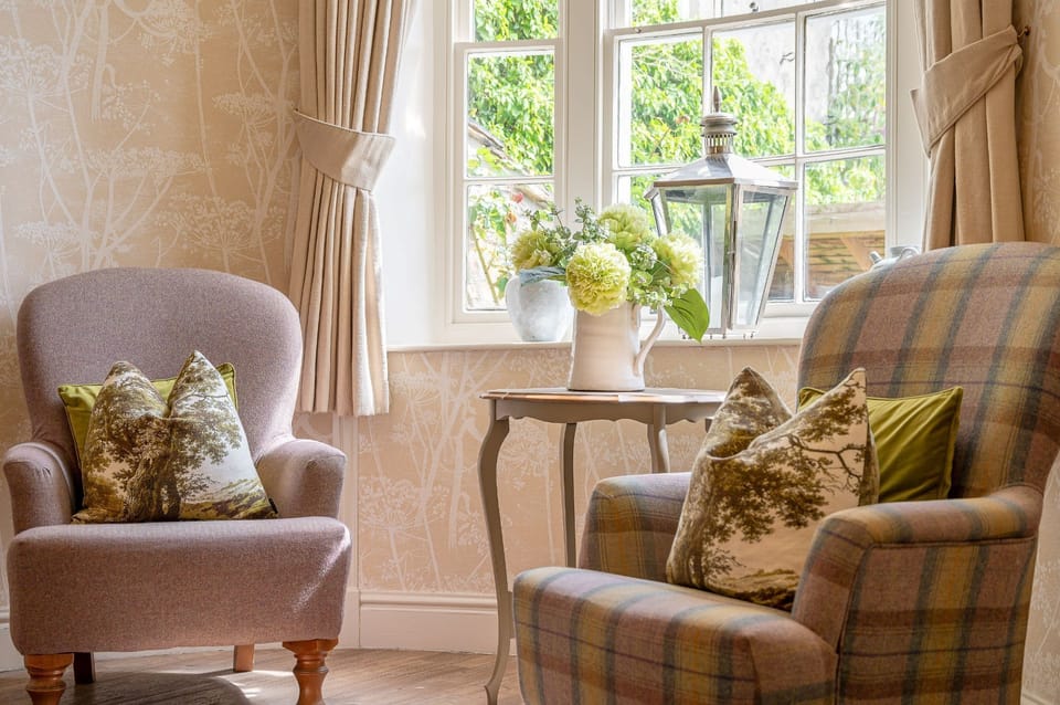 Sitting area at 30 Frenchgate with two armchairs, a small table with flowers, and a window with curtains and a lantern.