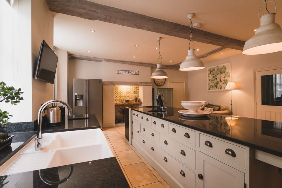 Kitchen at 30 Frenchgate with a long island and sink, pendant lights, exposed beams, and an inglenook-style cooker alcove with patterned tiles.