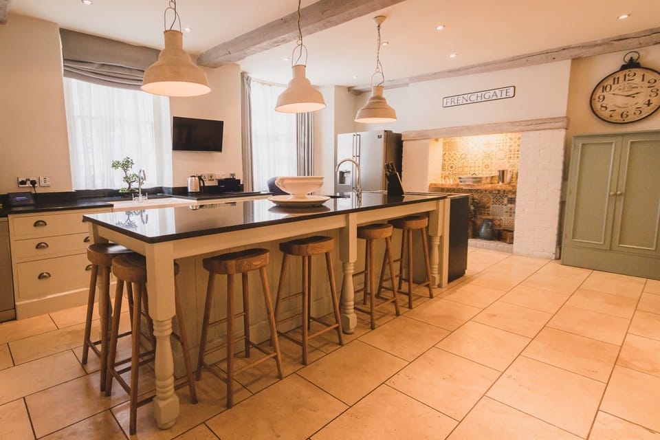 Kitchen at 30 Frenchgate with a large island and bar stools, pendant lights, and an inglenook-style cooker alcove with patterned tiles.