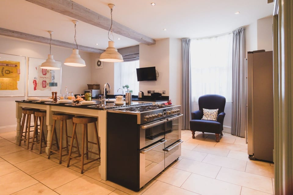 Kitchen at 30 Frenchgate with a large range cooker, island with bar stools, pendant lights, and a bay window seating area with an armchair.