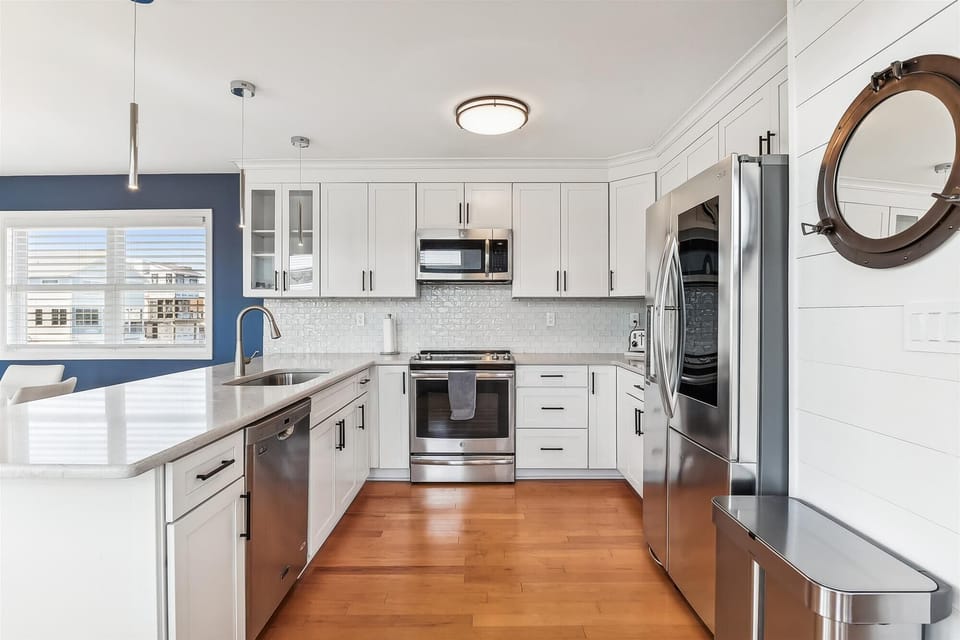 Your bright, modern kitchen awaits with sleek white cabinetry, stainless appliances, and a sunny breakfast bar—perfect for preparing fresh meals during your stay.
