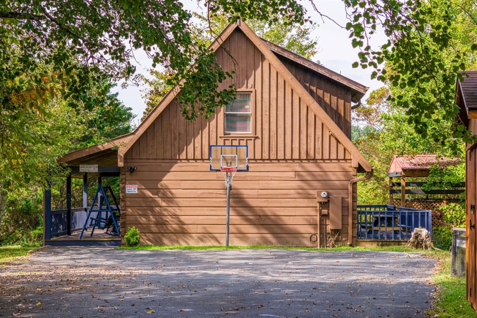 Charming wooden cabin nestled among towering trees with basketball court and playground nearby for active family fun.