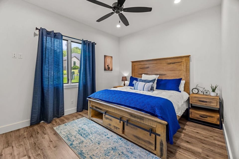 Bedroom with wood-frame bed, blue bedding, nightstands and window light.