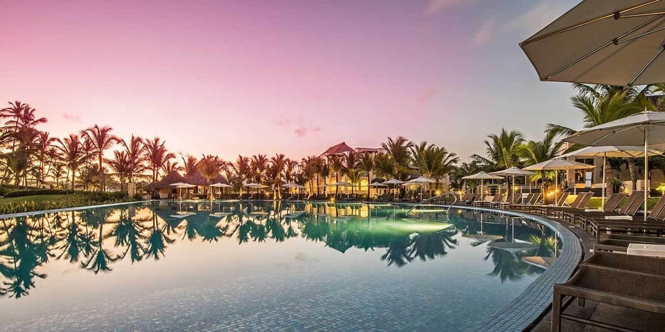 Sip cocktails poolside as sunset colors glow across water.