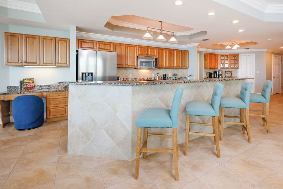 The kitchen features light wood cabinets, stainless steel appliances, and a granite countertop breakfast bar with blue stools