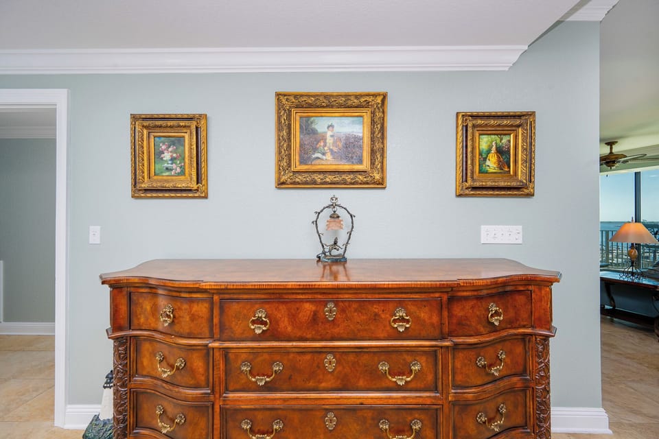 Wooden dresser with ornate details and framed artwork is displayed against a light blue wall in a stylish room