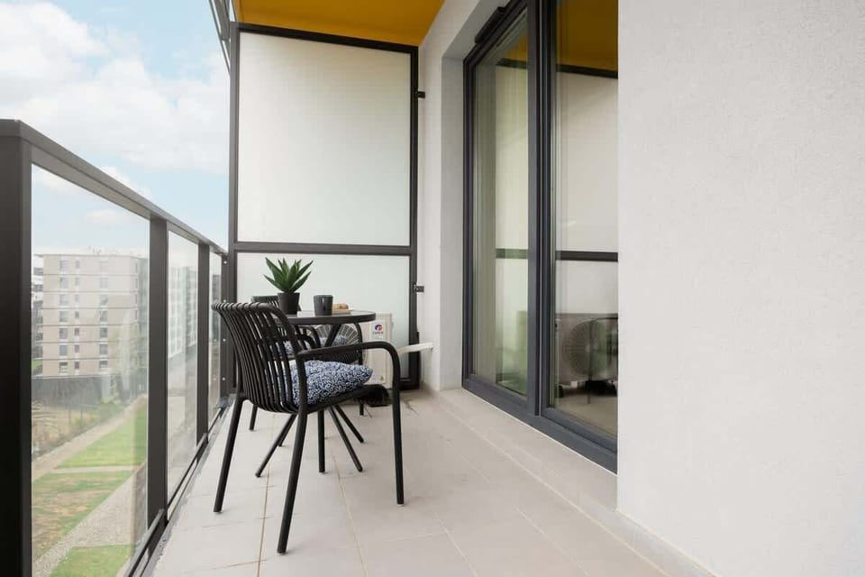 A bright balcony with a black table and chairs, surrounded by glass railings. A cozy outdoor spot for coffee or fresh air.