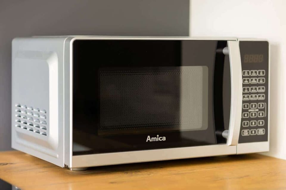A close-up shot of a microwave placed on a wooden surface. The microwave is black and silver, adding contrast to the kitchen decor.