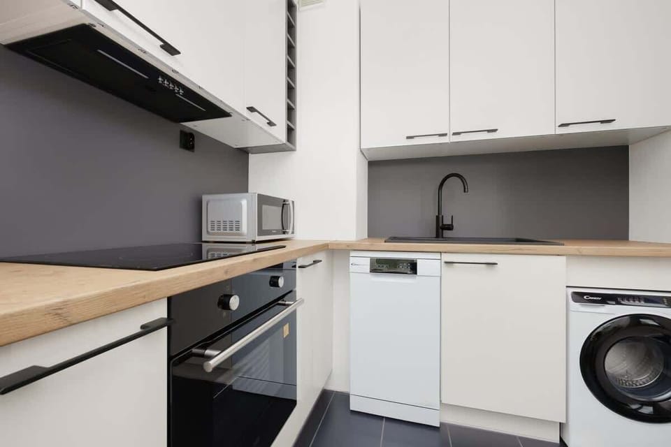 A modern kitchen with white cabinets, a built-in stove, and a washing machine. The kitchen area is neat and efficiently organized.