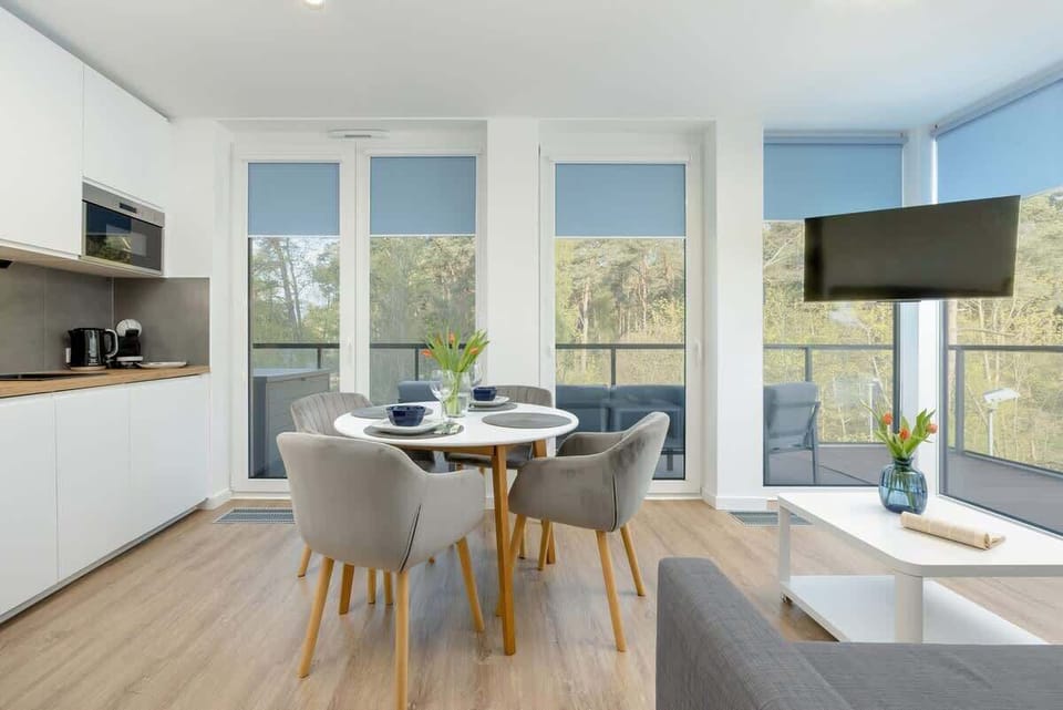  A modern kitchen with white cabinets, high quality domestic appliances and plants on the counter. The kitchen looks out onto a scenic view.