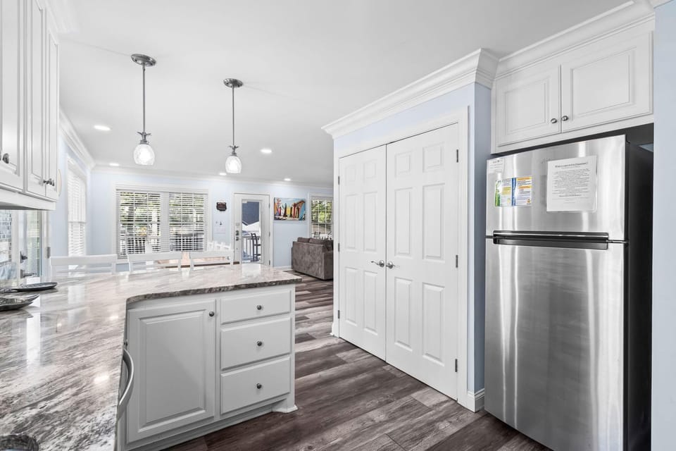 Granite countertop curves around the white cabinetry with a stainless steel refrigerator and wood-look flooring below.