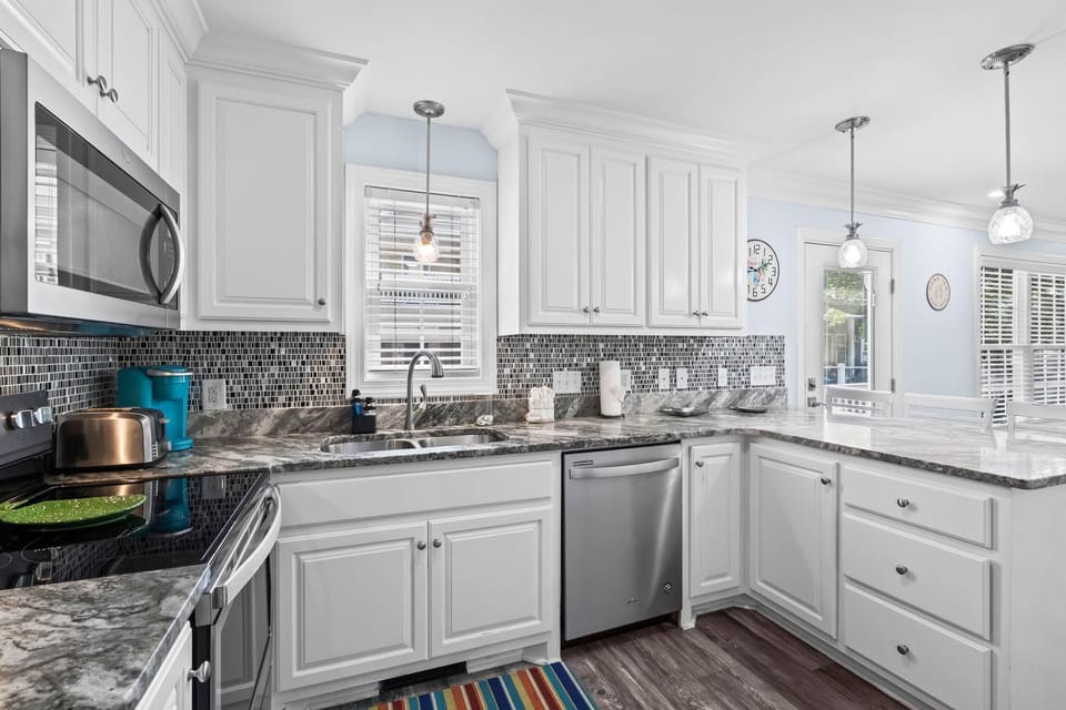 White shaker cabinets and gray granite counters surround stainless appliances in the kitchen.