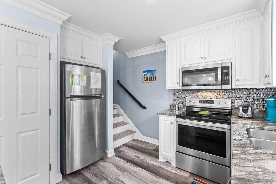 Stainless steel refrigerator and oven sit against white cabinetry with mosaic tile backsplash in kitchen corner.