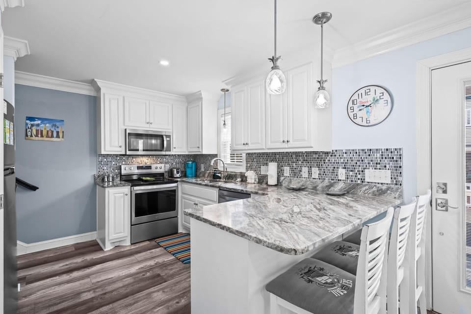 Marble-patterned countertops extend to a breakfast bar with cushioned white stools under glass pendant lights.