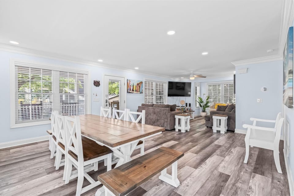 Dining area with white wooden chairs and a bench surrounding a rectangular table on gray plank flooring.