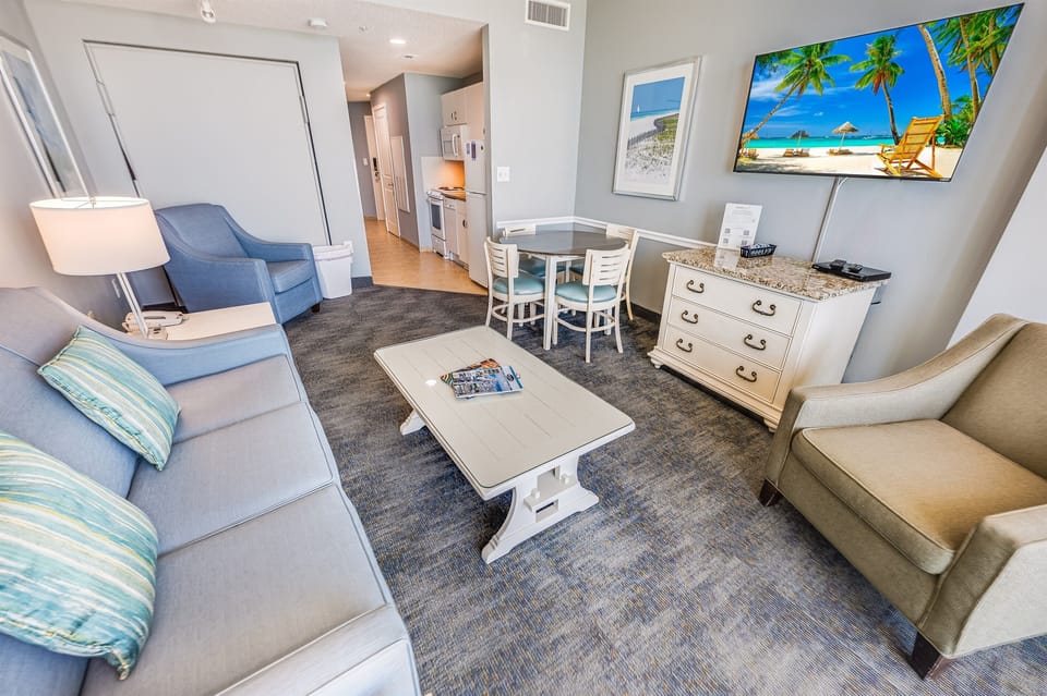 - Bright living room with sofa TV dining space and direct kitchen view   - Comfortable setup with modern decor and vacation style details   - Open plan design perfect for relaxing after the beach or pool