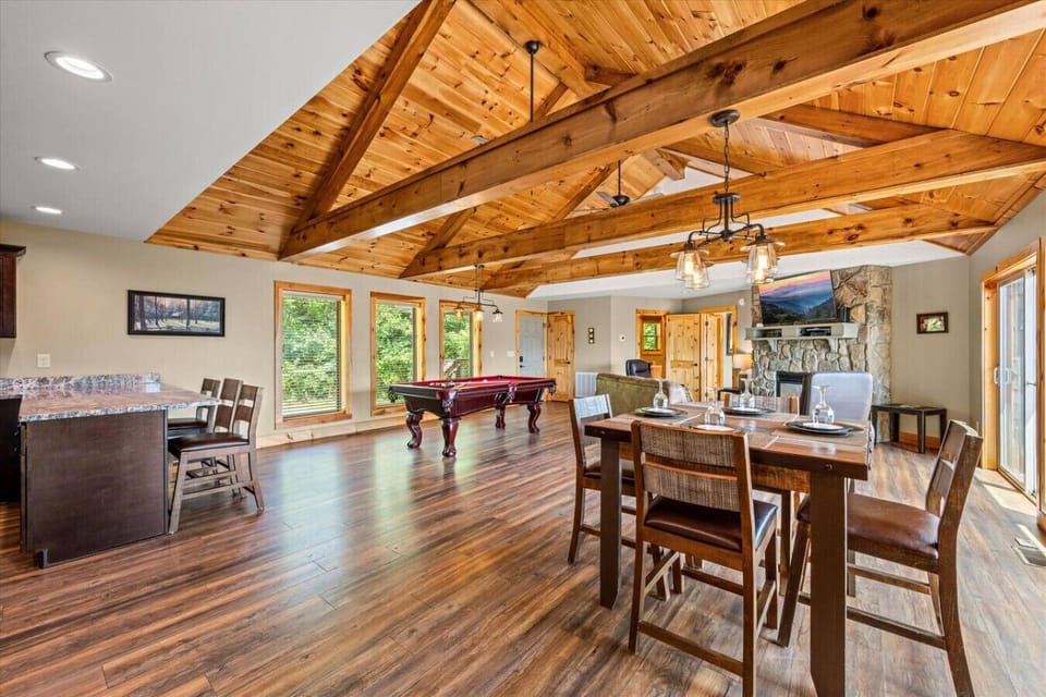 Vaulted ceilings with exposed beams, a stone fireplace, and warm wood floors create a space that feels both grand and inviting. Whether you’re dining, relaxing, or playing a round of pool, everyone stays connected.