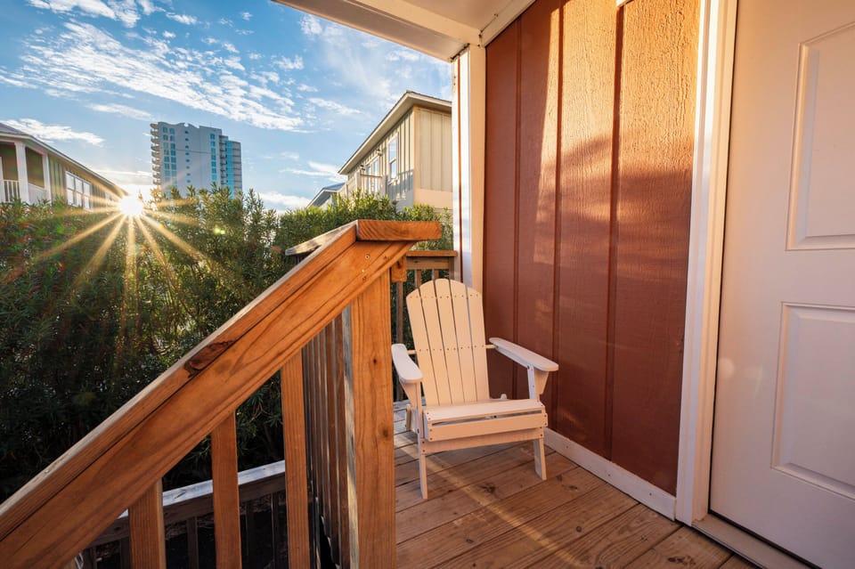 Sunset glow on a cozy porch with a white chair and lush greenery view.