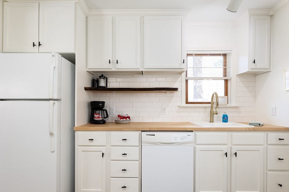 Our modern kitchen boasts white cabinets, wooden countertops, and an array of appliances, emitting a clean and organized atmosphere ideal for culinary exploration.