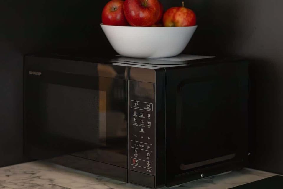 A kitchen countertop with a microwave and a bowl of apples on top. The scene is simple and functional.