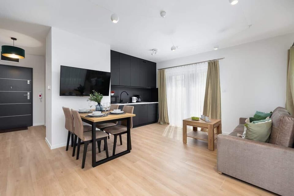 A living room combined with a dining area, featuring a gray sofa and large windows allowing plenty of natural light.