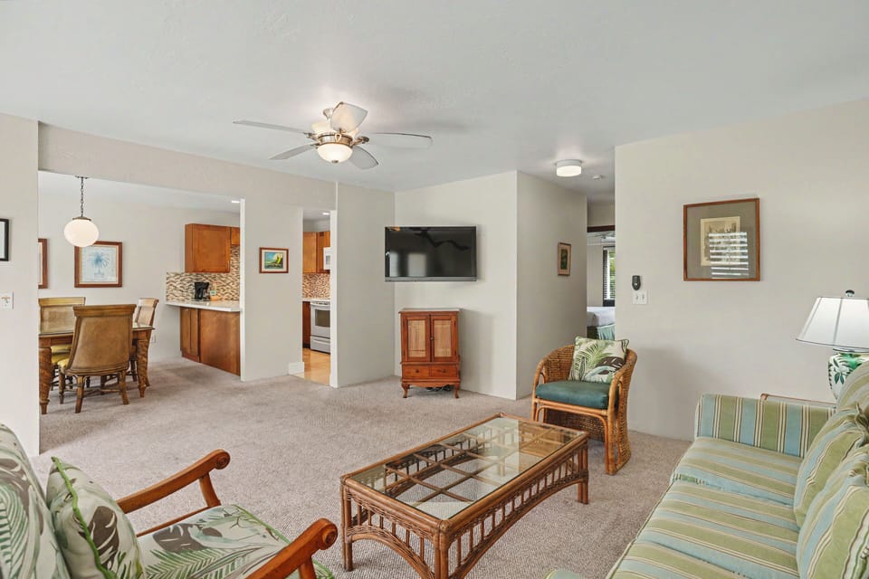 Picture yourself unwinding in this bright open living space with tropical touches and a gentle ceiling fan breeze. The kitchen is just steps away, and every corner invites you to settle in and relax.