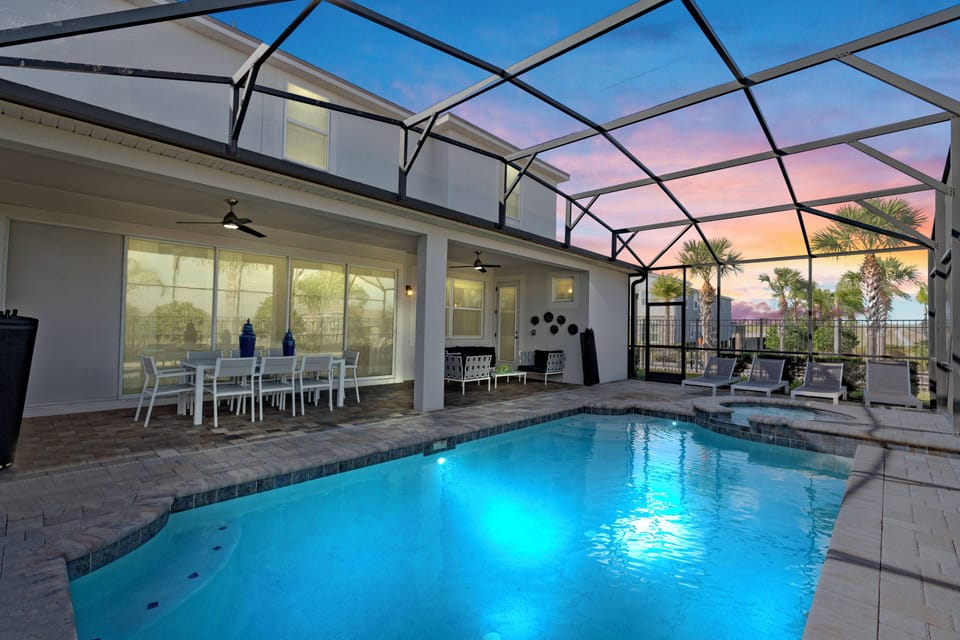 Step outside to a beautiful pool area with a sleek screened enclosure, where vibrant blue water mirrors the evening sky. Enjoy al fresco meals at the inviting dining set, framed by serene palm trees for a relaxing atmosphere.