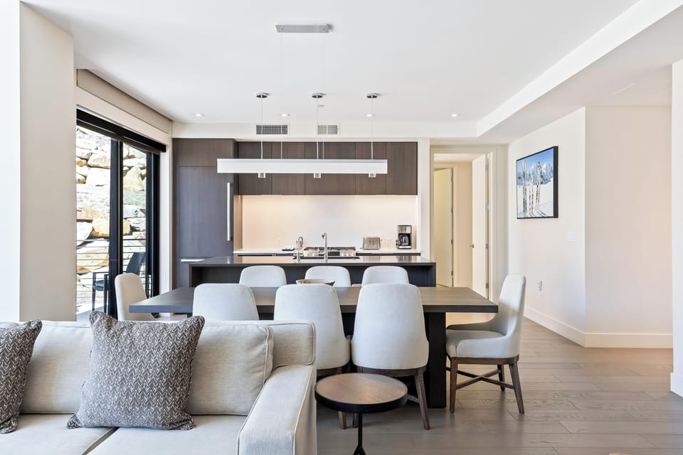 - Host dinners with ease at a sleek table that comfortably seats eight
- Modern kitchen features dark cabinetry, built in appliances, and pendant lighting
- Seamless flow from kitchen to living area makes entertaining effortless