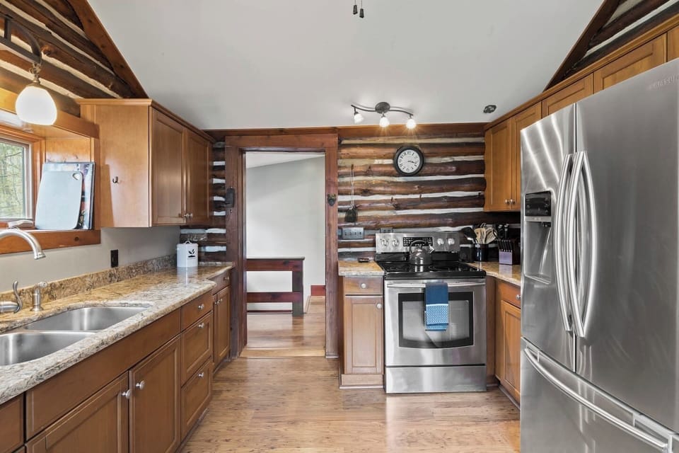 Kitchen (second floor)- This well-appointed kitchen features high-quality stainless steel appliances, granite countertops, and ample wooden cabinetry, set against a backdrop of rustic log walls for a homely yet sophisticated feel.
