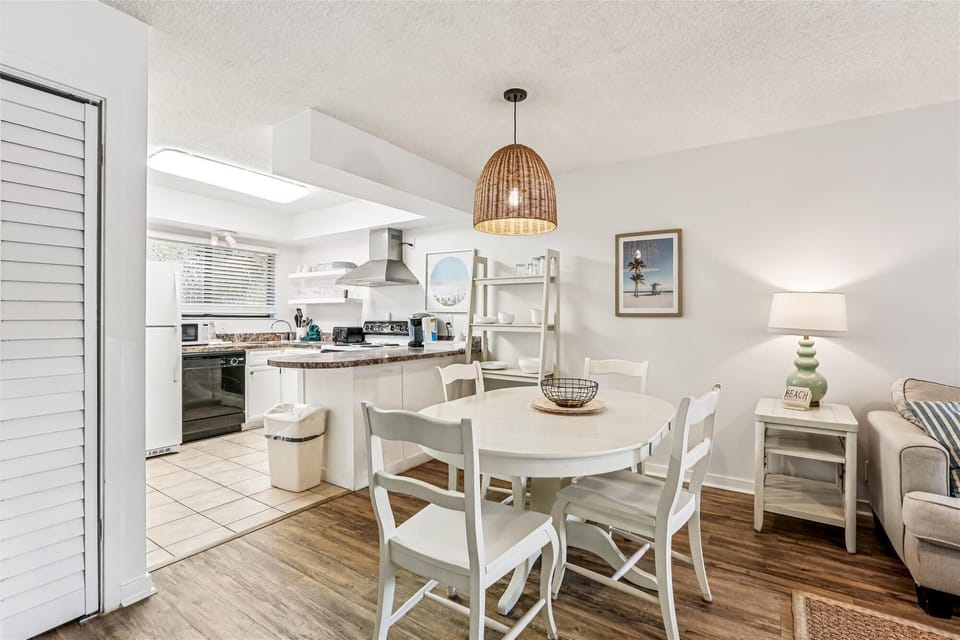 - Dining space with round table and chairs set beneath a woven pendant light
- Open floor plan connects to living room and kitchen for convenient gatherings
- Bright decor and coastal artwork create a cheerful welcoming setting