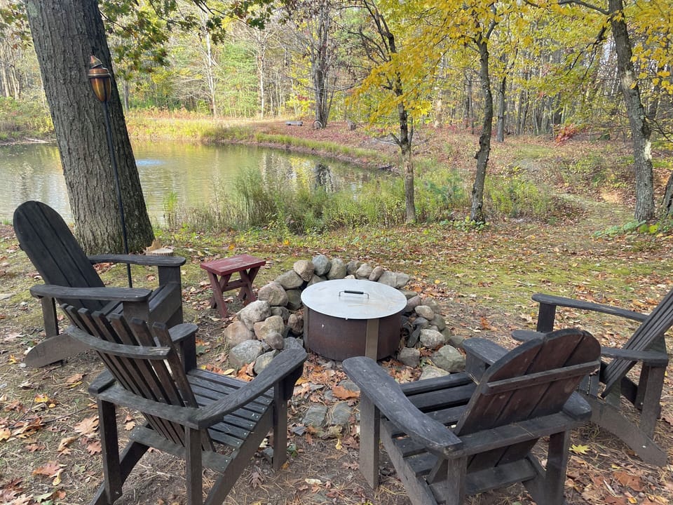 Adirondack chairs by the picnic table, all-season fire pit and pond.