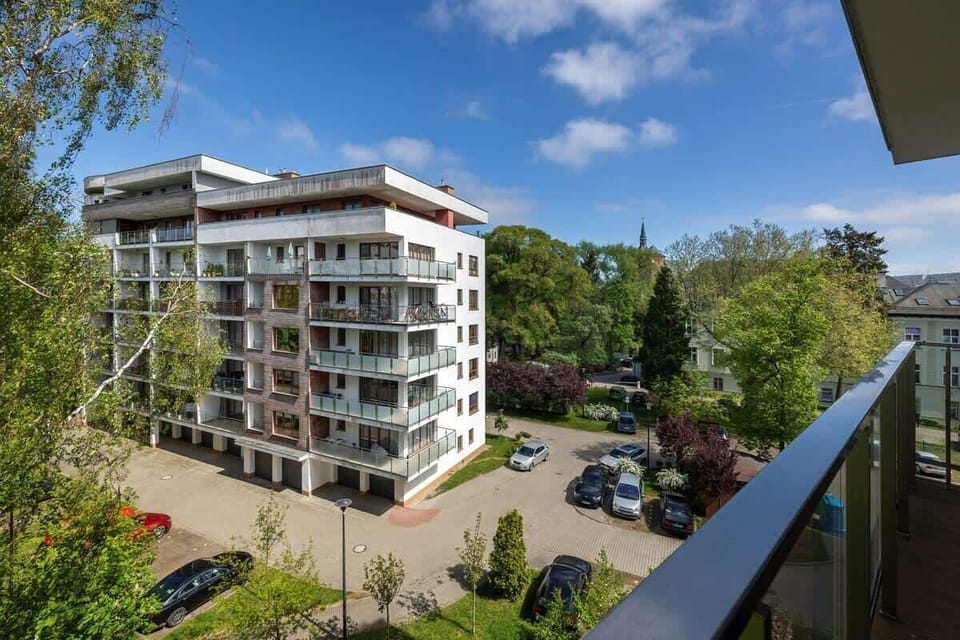 A view of a residential complex surrounded by greenery on a sunny day shows the peaceful and well-maintained surroundings of the apartment.