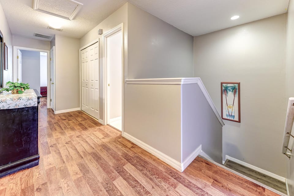 Hallway with wood-look flooring, white trim, closet doors, and staircase leading down with palm tree artwork.