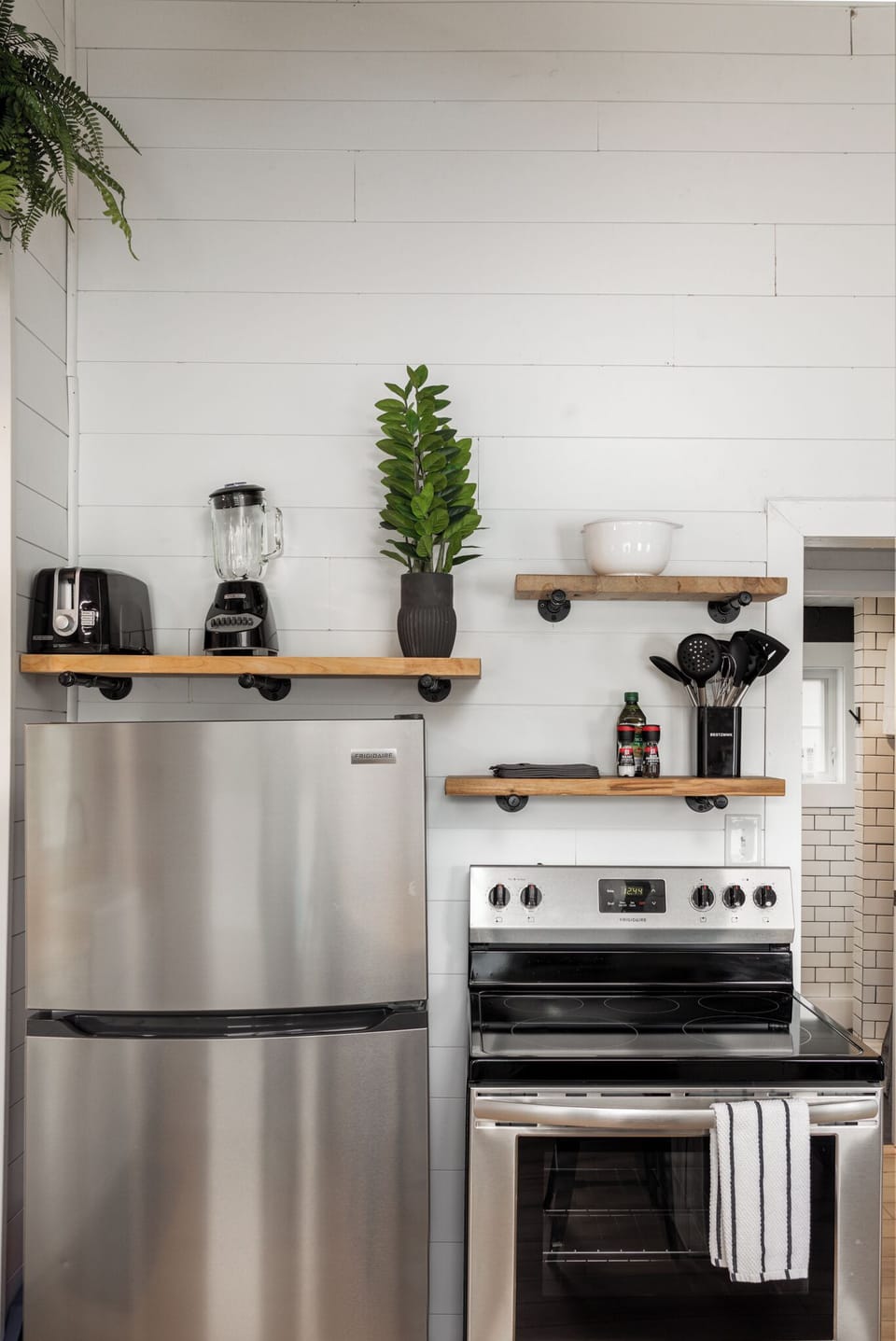 Sleek kitchen corner w/ stainless steel fridge, open shelves & coffee station.