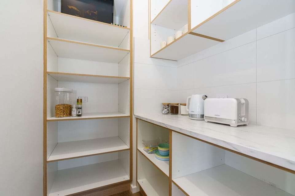 Experience elegance and functionality in this pristine pantry, featuring sleek white cabinets and shelves.