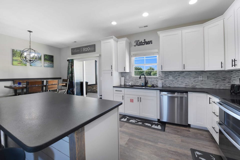 Modern kitchen with white cabinetry, black countertops, and a dining area with natural light.