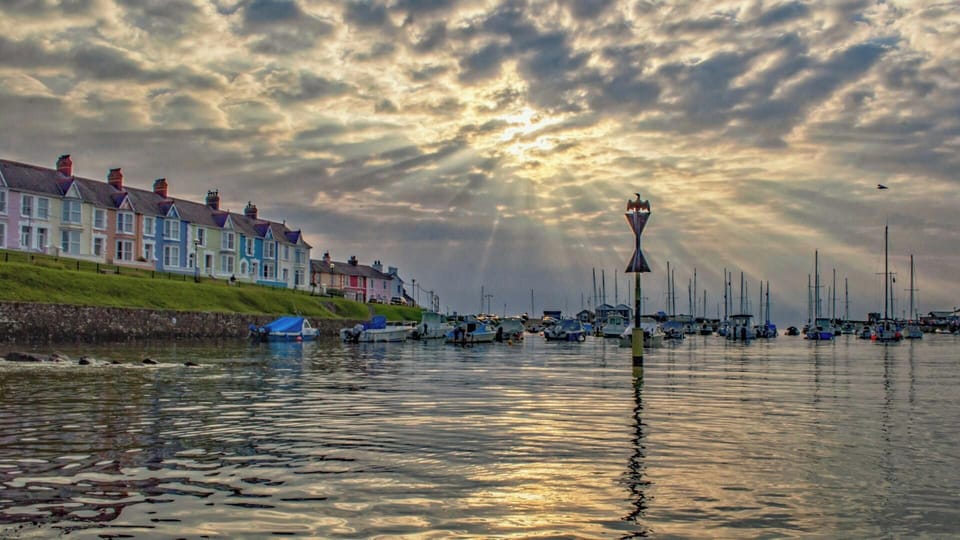 Bronze statue of a kneeling woman with outstretched hand overlooking New Quay harbour
