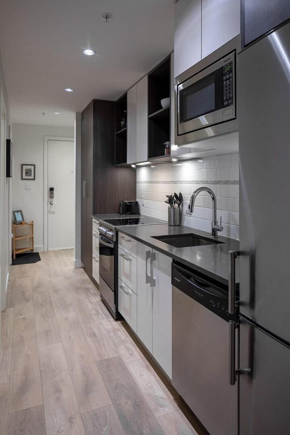 A long-angle perspective down the modern kitchen aisle, emphasizing the seamless built-in microwave and stainless steel appliances.