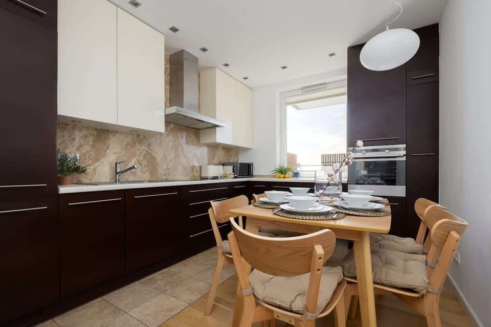 A modern cooking and eating space with sleek cabinetry, bright lighting, and wooden chairs.

