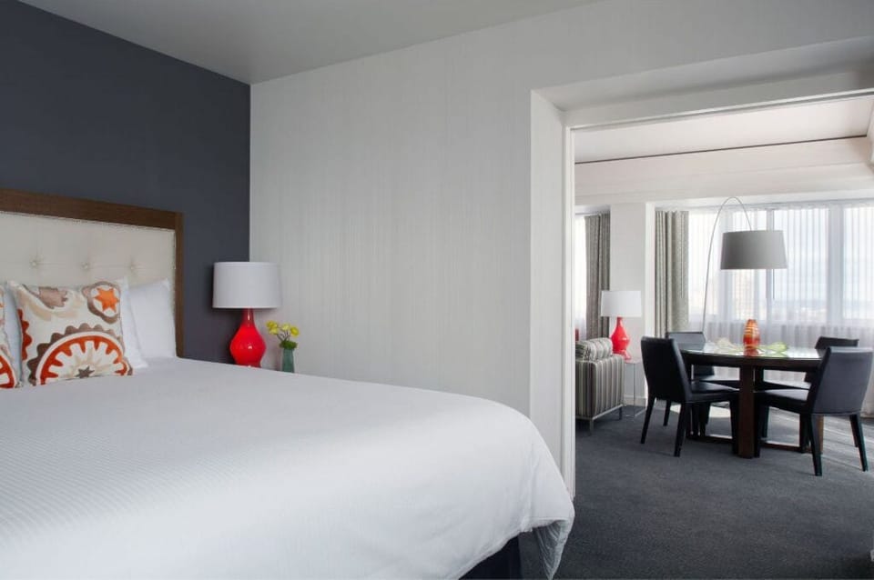 Minimalist bedroom with crisp white bedding, vibrant accents, and a dining area.