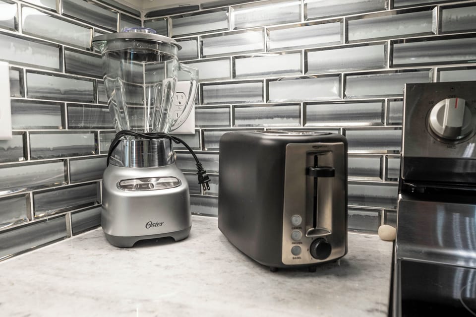 Sleek kitchen corner with modern toaster, blender, and glossy tile backsplash.