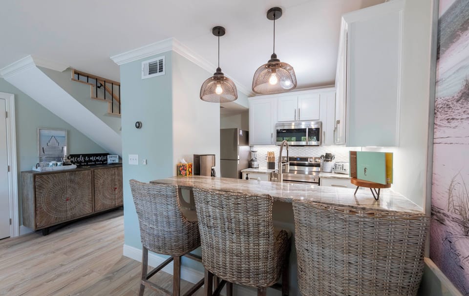Modern kitchen with wicker stools, pendant lights, and steel appliances.