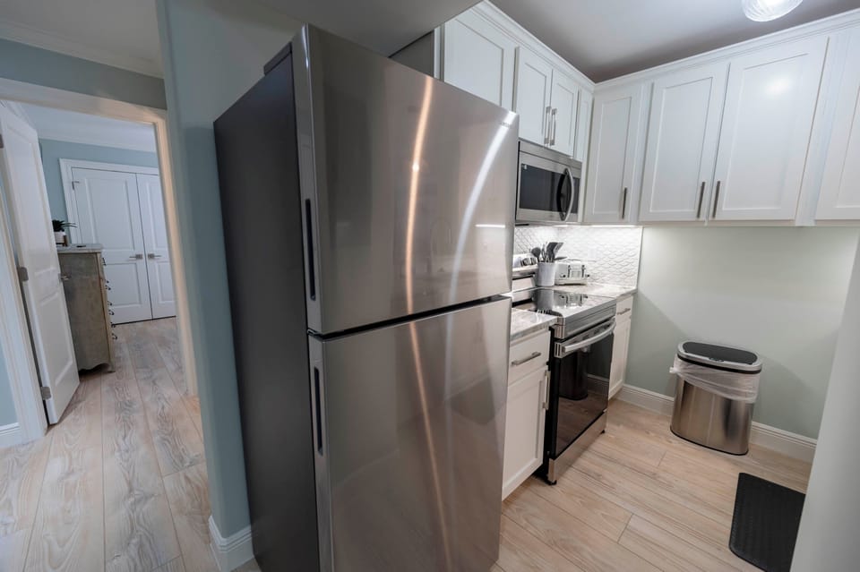 Modern kitchen: white cabinets, stainless steel appliances, warm wood floors.